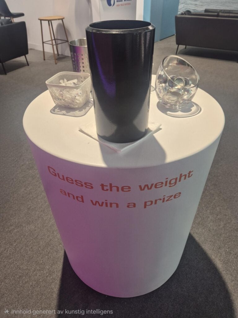 Black cylindrical container on a white table with glass objects and a sign.